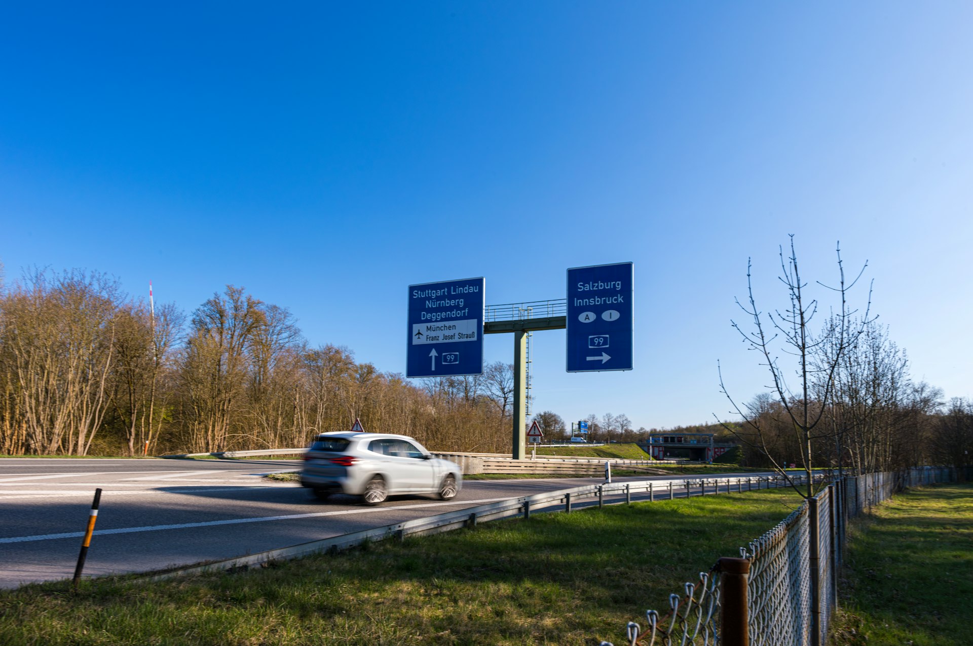 Car drives under highway signs on a sunny day.